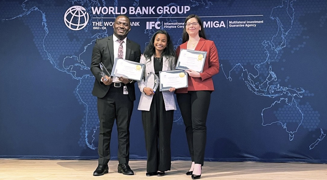 GW students Era Andriambololona, Anja de Waal and Seth Amo-Nyarkoh pose in front of a World Bank Group backdrop after winning the 2024 IFC Impact Challenge