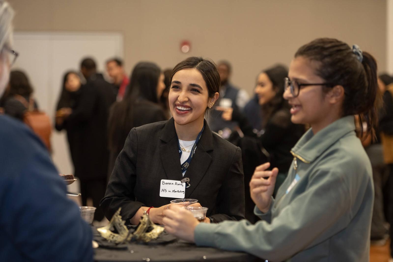 two students smile while in conversation with an alumnus at a networking event