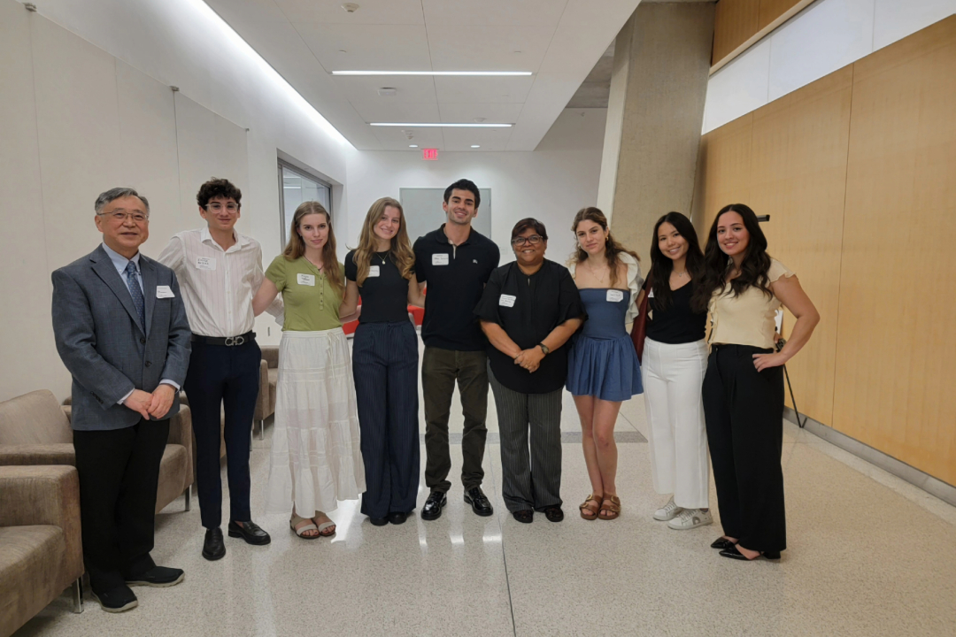 A group of people stand in a hallway for a photo. They are dressed in business attire.