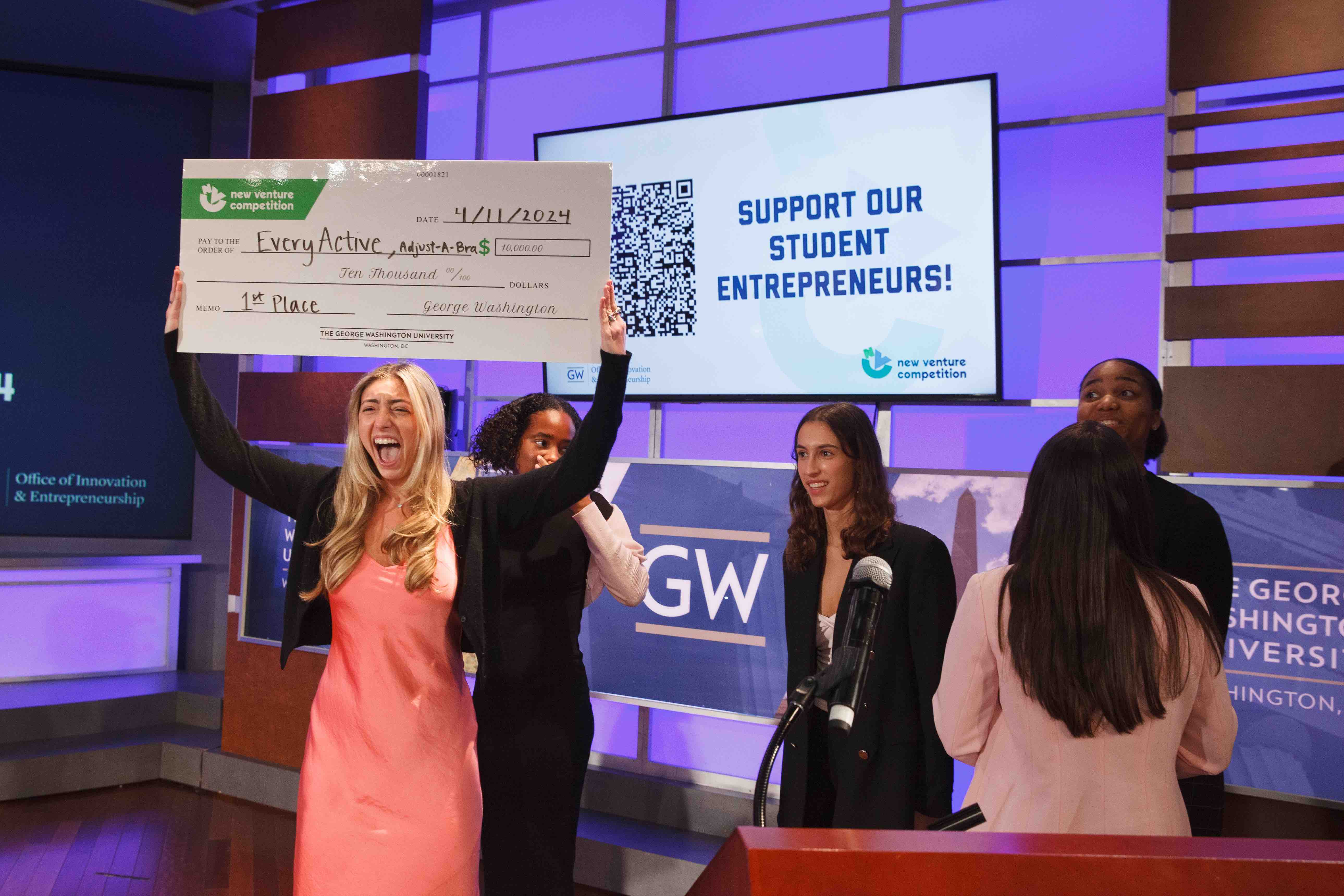 Camryn Baum celebrates her New Venture Competition win onstage, holding up her oversized check for $10,000.