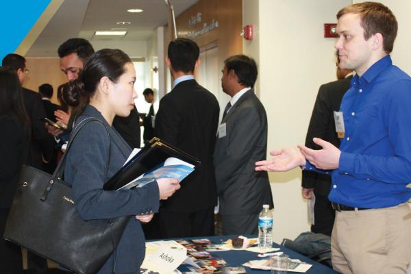 Person in blue button up talking to person in blazer holding binder