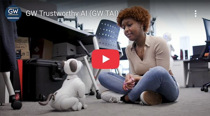 screenshot from GW Trustworthy AI video shows a woman seated cross-legged on the floor interacting with a robotic pet dog