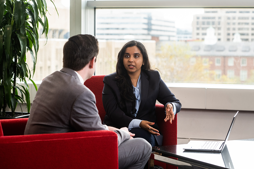 two GWSB students in business attire chat at a table in Duques Hall
