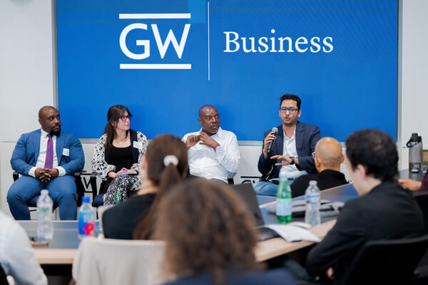 4 panelists sit at front of room under GW Business sign at an AI Business Society event