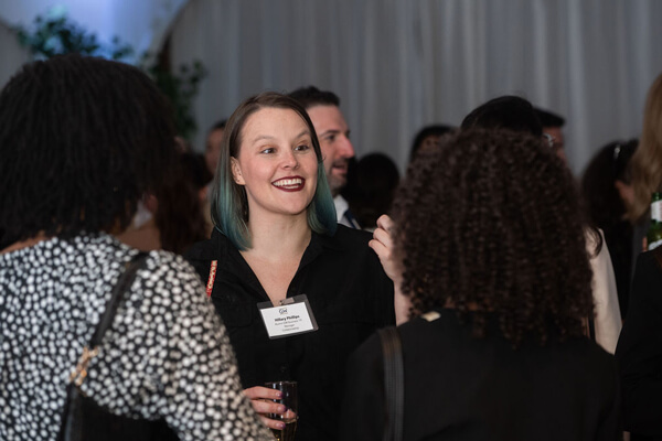 Attendee smiles while talking to two colleagues with their back to camera at mixer event