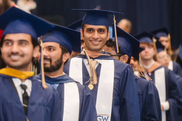 Business School grad smiles at camera while in commencement processional
