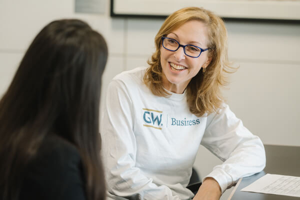 Career Center staff member wearing shirt with a "GW Business" logo on it smiles while talking to student