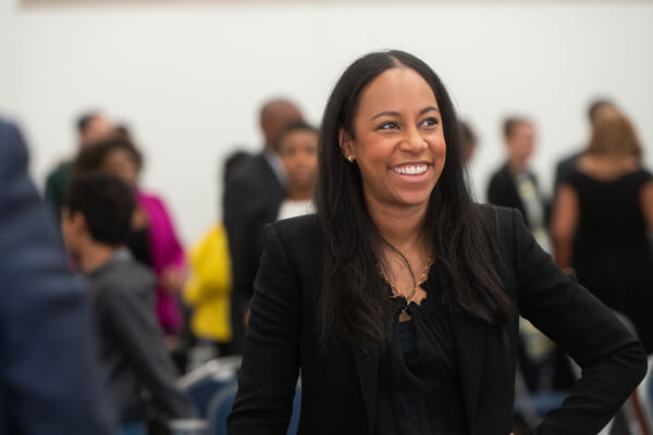 professional female smiles toward someone off-camera, group of professionals blurred in the background