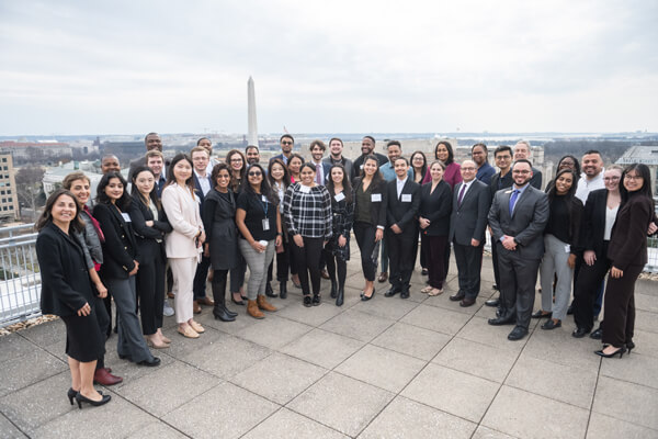 large group of professionals pose for photo on rooftop, Washington Monument in the distance