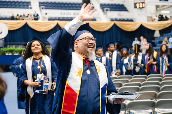GW graduate smiles and raises his hand to wave to someone during Commencement procession