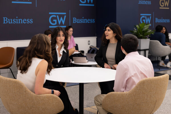 group of GW Business students seated at small round table talking