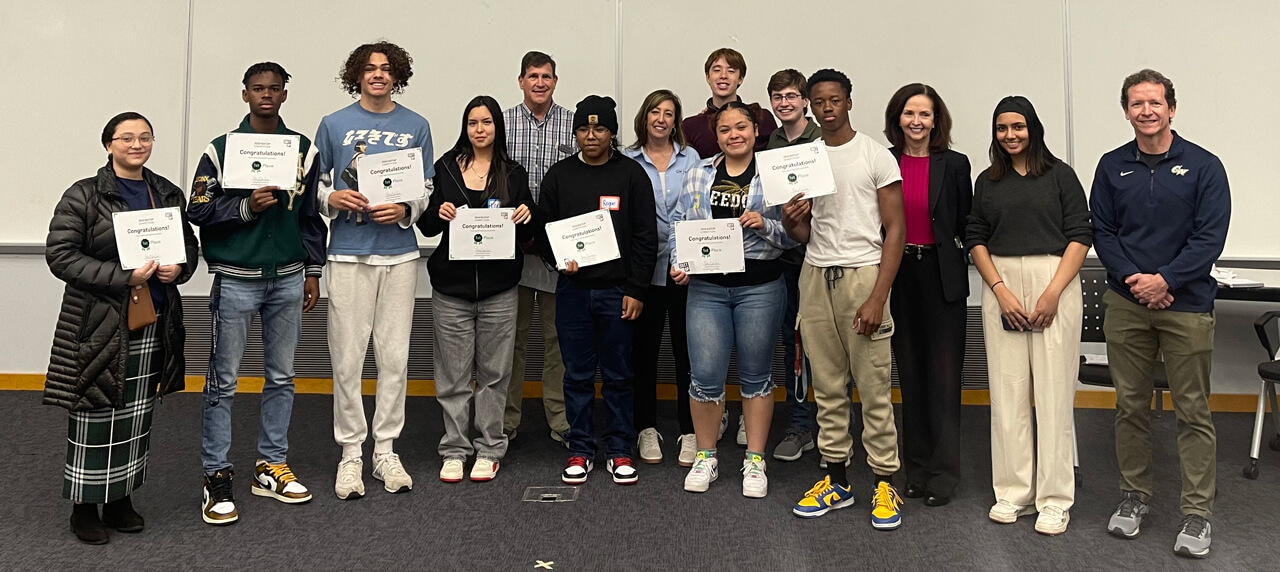 A group of students stands together indoors for a photo. They smile and hold certificates. 
