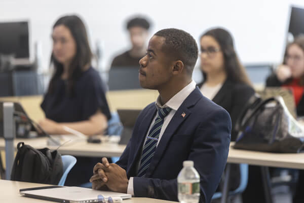 Professional male listens intently in classroom, other students seated in the background