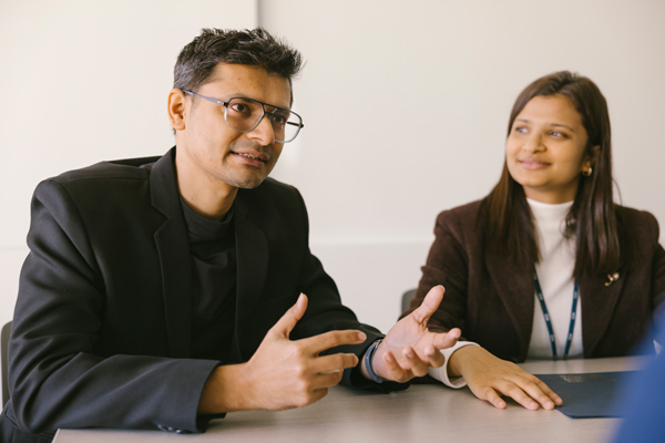 two professionals seated at table, one is talking to someone off camera
