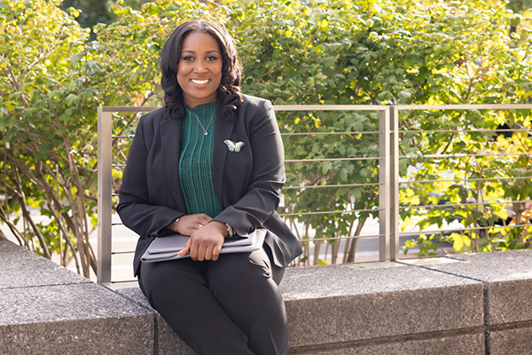 student sits on stone wall outside, bushes in the background, laptop closed in her lap
