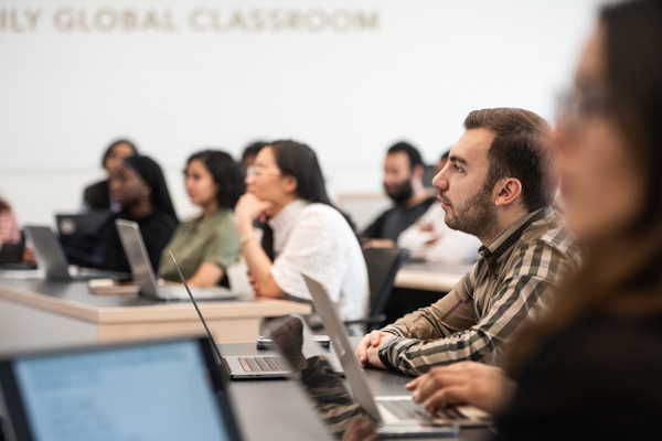 students listen intently in class, laptops in front of them on desks