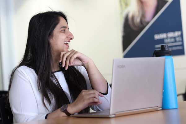 student smiles at someone off camera, laptop open on the desk in front of her