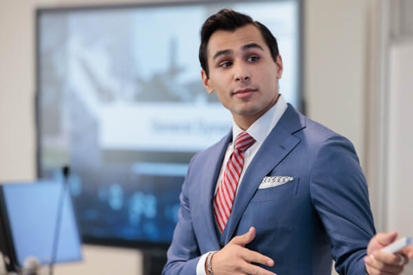 student dressed in business suit gestures toward presentation that is off-camera