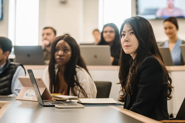 diverse students listen intently in class, laptops or tablets open in front of them