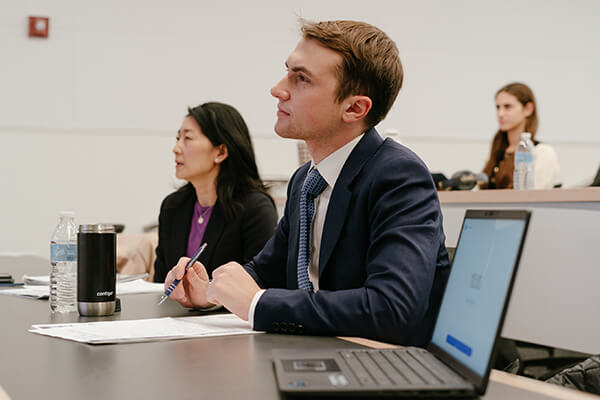 students in class listen to professor, laptop is open to the side of one student