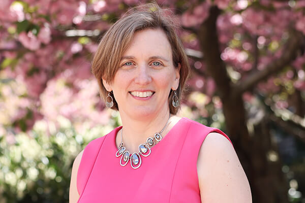 business student wearing pink top smiles at camera, cherry trees blurred in the background