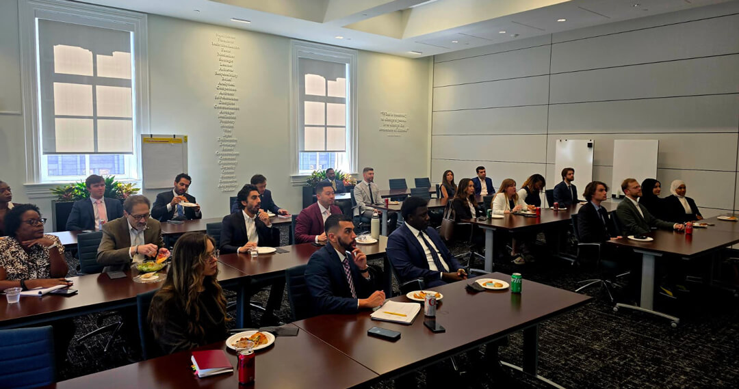 students sit in classroom style room eating lunch while listening to the speaker