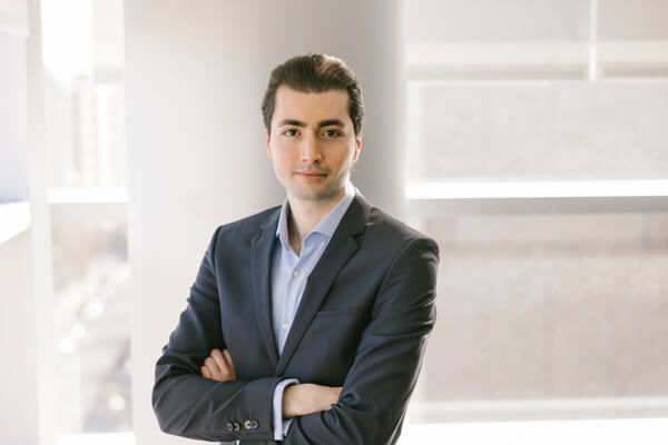 business student wearing business suit with arms crossed looks directly at camera, large column in background