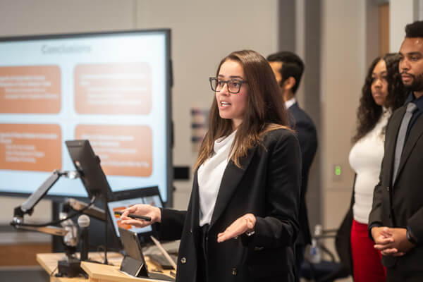 small group leads presentation in front of classroom, female in front speaking