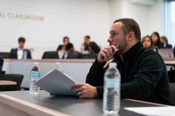 student listens intently in class, holds packet of paper in his hand