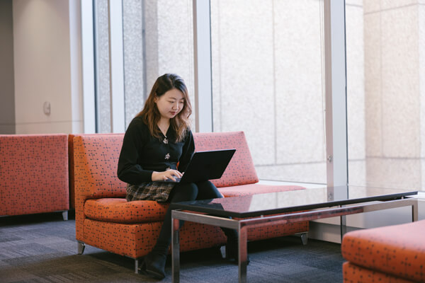 student works on laptop in lobby area with orange couches