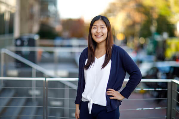 business student poses for photo outside, railings and trees in the background