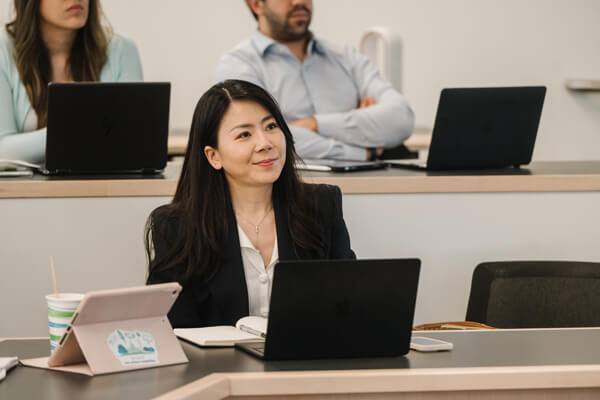 student listens in class, slight smile on her face, other students in the background