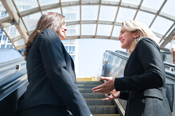 two professionally dressed females talk while riding up escalator exiting the metro station