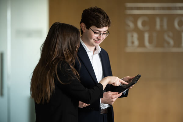 two business students look at tablet that the male student is holding, female points at screen