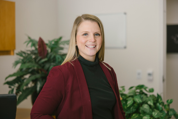 professionally dressed female smiles at camera in office, plants in background
