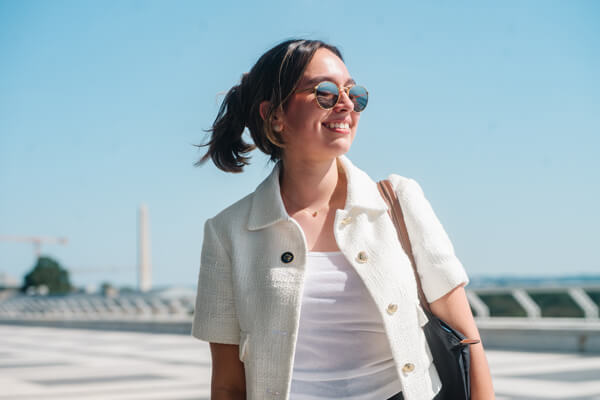 student wearing summer professional attire and sunglasses walks outside on a clear sunny day, Washington Monument in the distance of the background