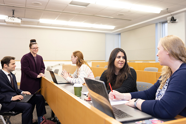 group of students collaborate in classroom, laptops open in front of a few of the, one standing