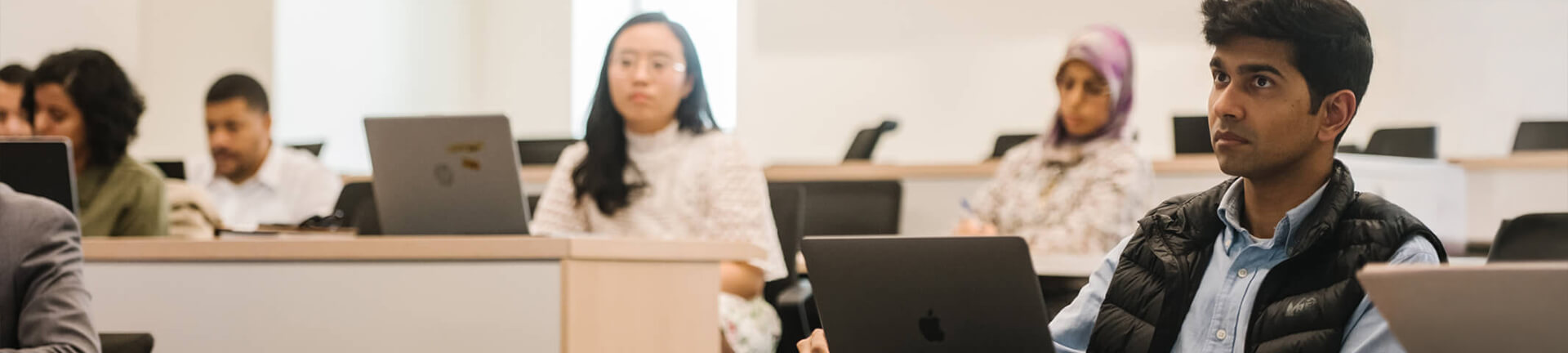 students in classroom listening intently, laptops open in front of them