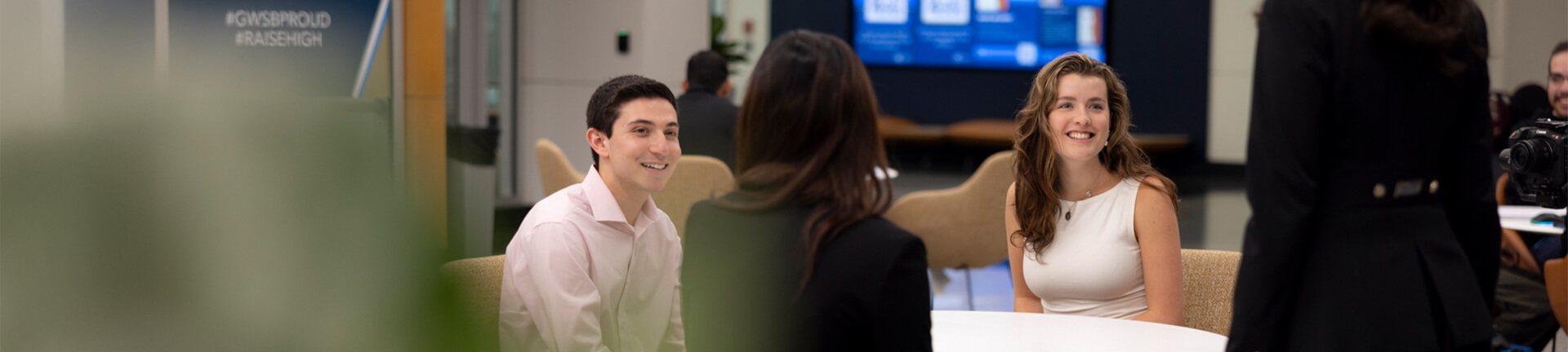 a group of 4 students chat around a round table in the business school lobby