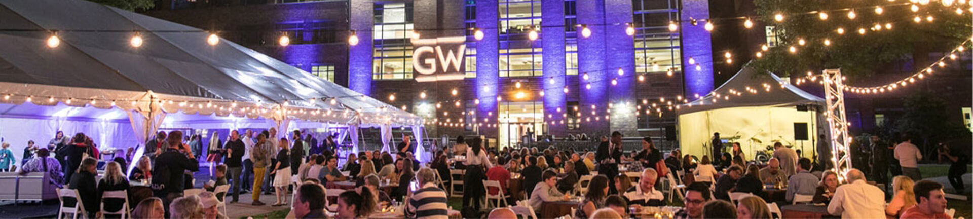 attendees gather during the evening at tables and under tents at a GW event in the University Yard 