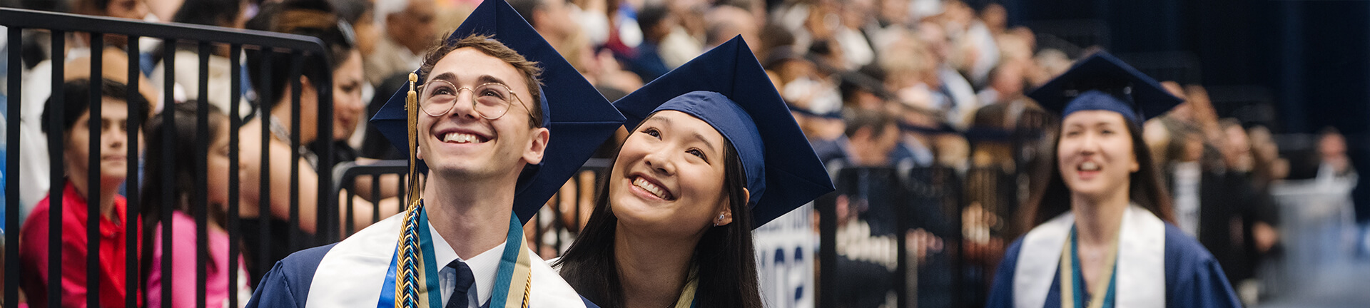two graduates smile toward the audience at commencement ceremony