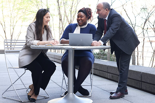 three professionals gathered around an outdoor table, laptop open in front of one