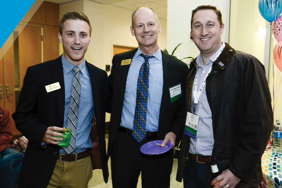 three alumni, dressed professionally, smile for photo together at event
