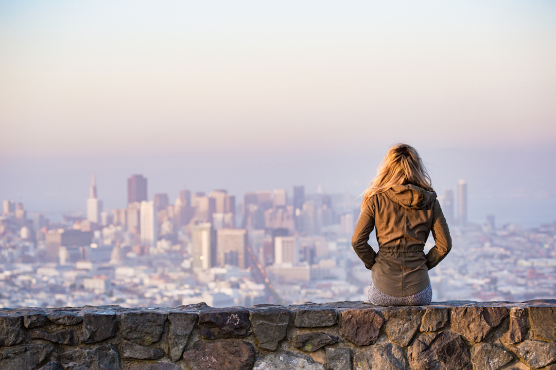 Woman with back turned looks at city skyline in distance.