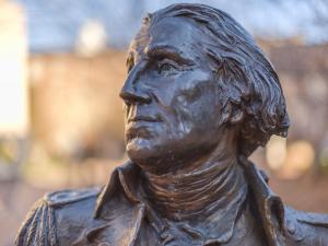 Image shows a broze statue of President George Washington with the GW University campus in the background.