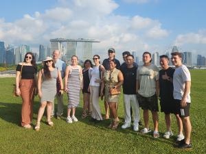 Students in GW's Global Bachelor's Program pose for a photo on a grassy lawn in Singapore. The city skyline with the iconic Marina Bay Sands Hotel is visible in the distance behind them. 