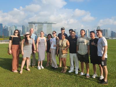 Students in GW's Global Bachelor's Program pose for a photo on a grassy lawn in Singapore. The city skyline with the iconic Marina Bay Sands Hotel is visible in the distance behind them.
