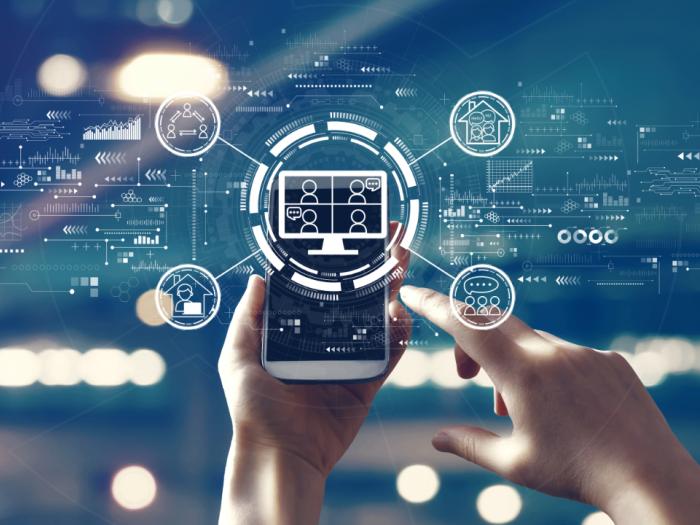 A person's hands appear, holding a smartphone. Icons beam from the smartphone screen, illustrating human and technology interaction.
