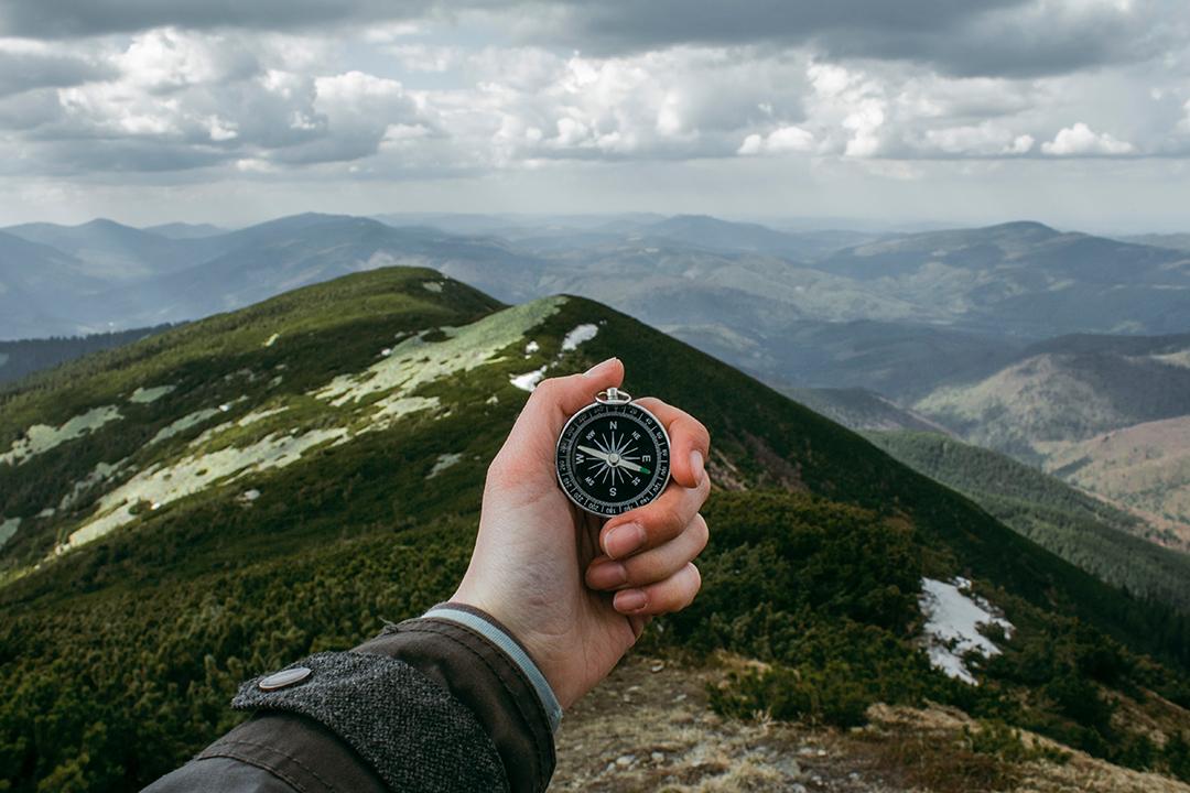 image shows a man holding a compass and navigating from the top of a mountain