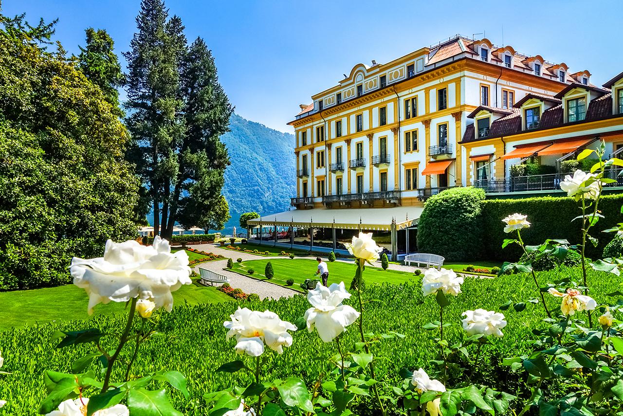 spring flowers are visible in the foreground of this garden view of the Villa d'Este on Lake Como in Cernobbio, Italy